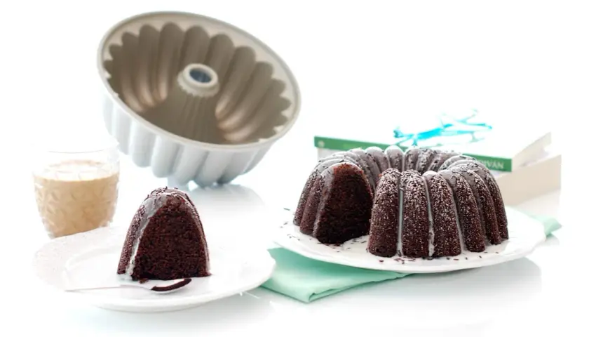 Bizcocho chocolate Thermomix, recién horneado y decorado con glaseado blanco. Un trozo ya servido con un vaso de leche.