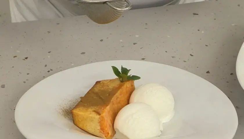 Un trozo de flan de calabaza Arguiñano, espolvoreado con canela, acompañado de dos bolas de helado de vainilla y una hoja de menta.