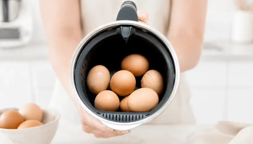 Manos sostienen el recipiente de la Thermomix lleno de huevos, listos para cocer huevos thermomix.