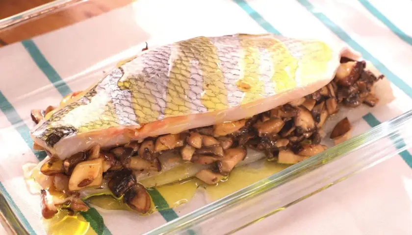 Pescado relleno de setas al horno, jugoso y dorado, listo para servir en una fuente de cristal.