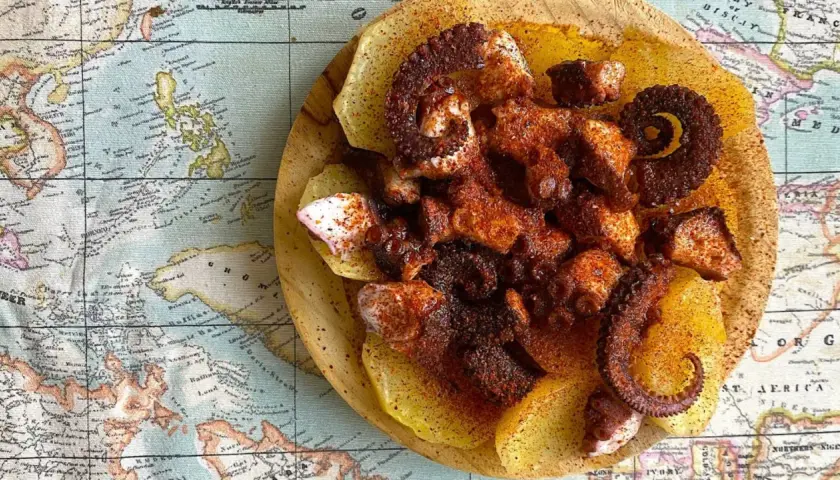 Pulpo con patatas, un plato gallego servido sobre un mapa antiguo. Tentáculos de pulpo especiados y tiernos sobre rodajas de patata.