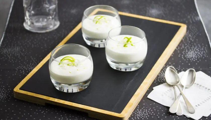 Tres vasitos de cremoso mousse de limón, decorados con ralladura verde, listos para disfrutar.
