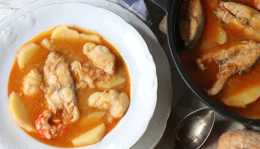 Un delicioso suquet de pescado con patatas y gambas, servido en un plato blanco y una cazuela.