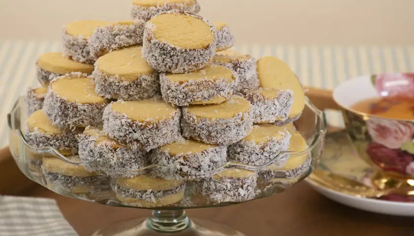 Montón de alfajores de maicena cubiertos de coco rallado, apilados en una fuente de vidrio.