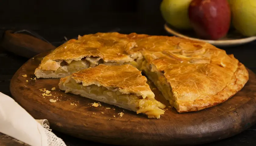 Empanada de manzana de la abuela, dorada y casera, servida en tabla de madera.