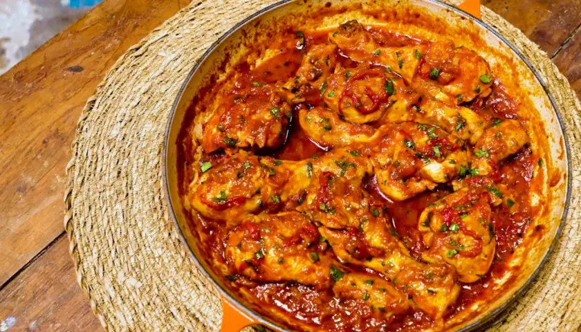 Pollo en salsa roja, como las recetas de pollo en salsa de la abuela, servido en cazuela naranja sobre esterilla de mimbre.
