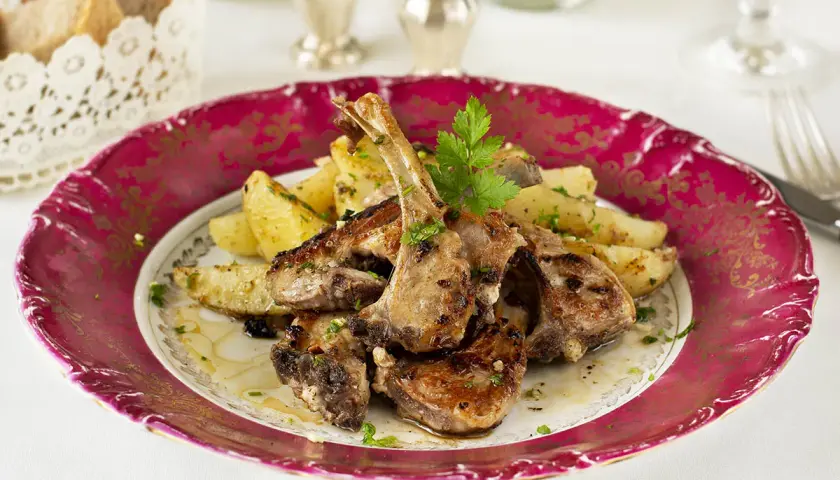 Chuletillas de cordero jugosas y doradas, acompañadas de patatas asadas y perejil fresco, servidas en un plato elegante.