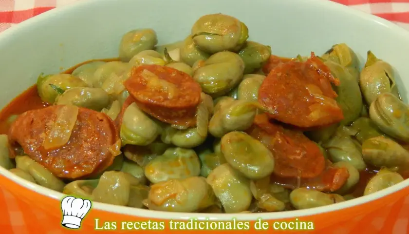 Un plato humeante de habas tiernas con rodajas de chorizo español, todo bañado en una salsa sabrosa.