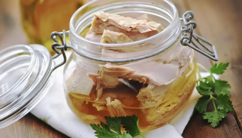 Un frasco de vidrio con atún en escabeche, listo para disfrutar. Unas hojas de perejil adornan la escena.