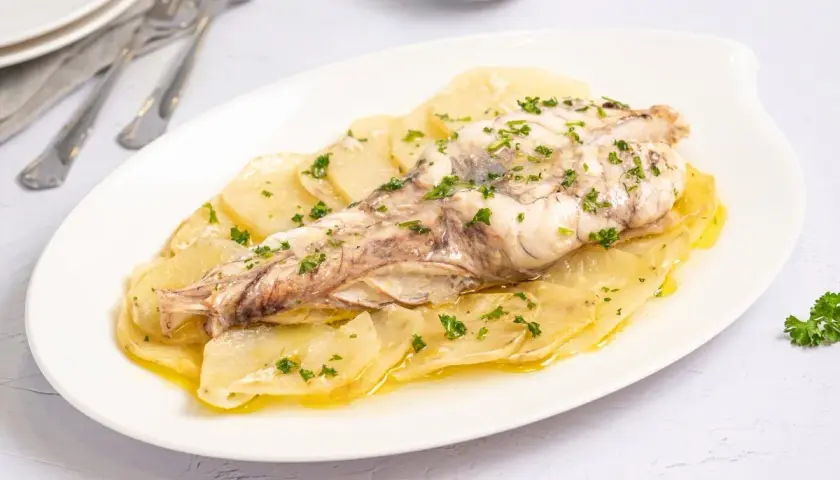 Rape al horno servido sobre patatas laminadas y espolvoreado con perejil fresco. Un plato sencillo y delicioso.