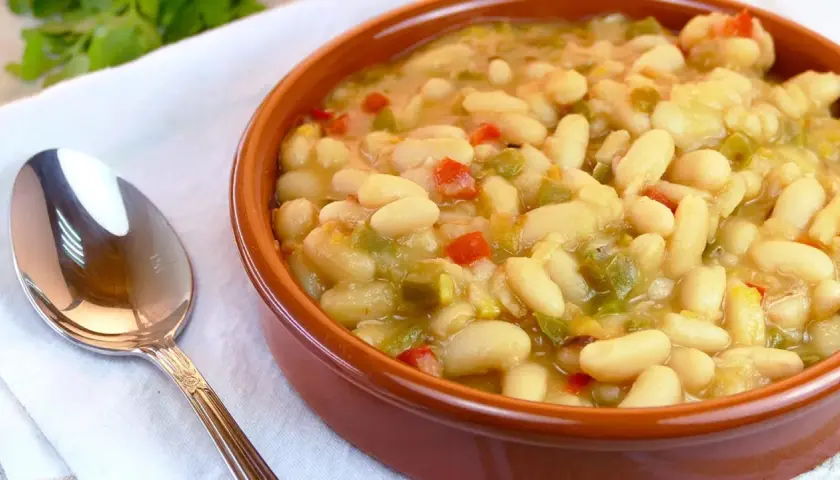 Judías blancas de bote salteadas con pimientos y cebolla, servidas en cuenco de barro.