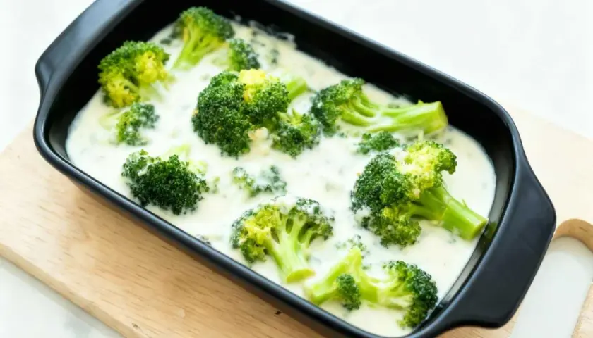 Brocoli con bechamel cremoso en una bandeja negra, listo para hornear. Un plato reconfortante y delicioso.