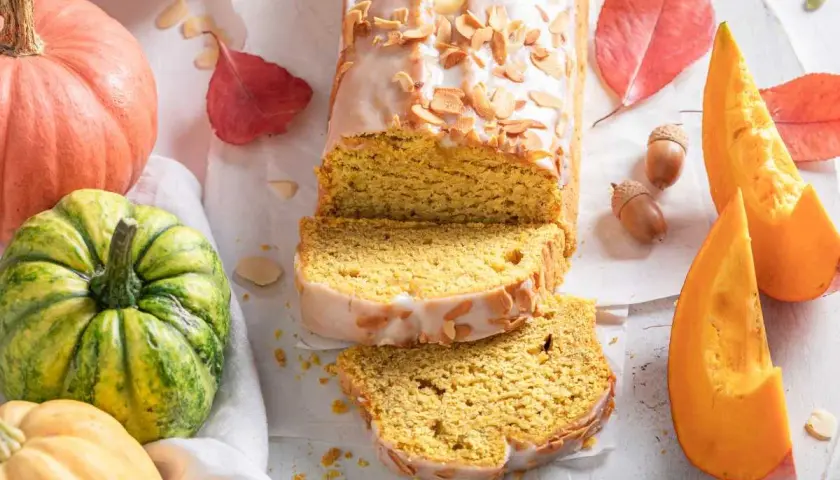 Bizcocho de calabaza Thermomix cubierto de glaseado y almendras. Rodeado de calabazas, hojas de otoño y bellotas.