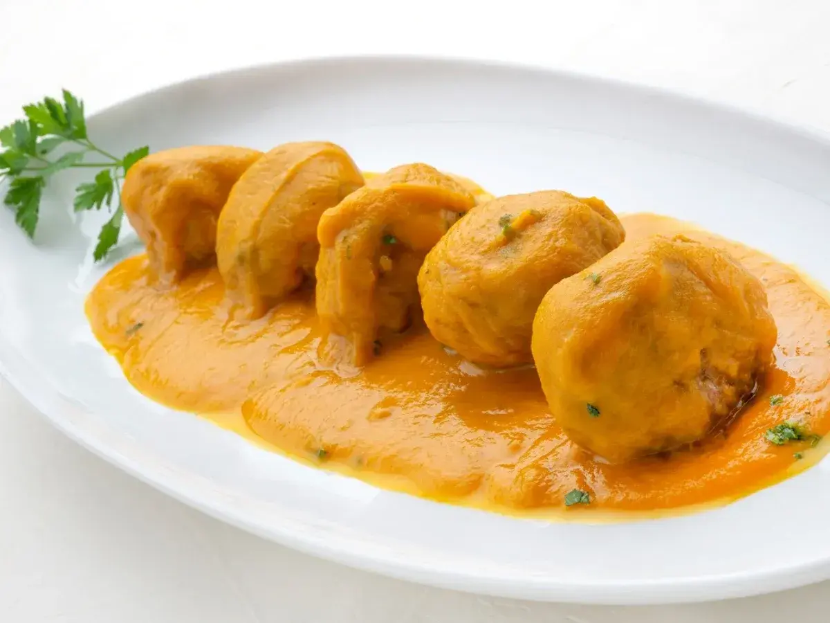 Cinco albóndigas en salsa arguiñano, servidas en un plato blanco con perejil fresco.