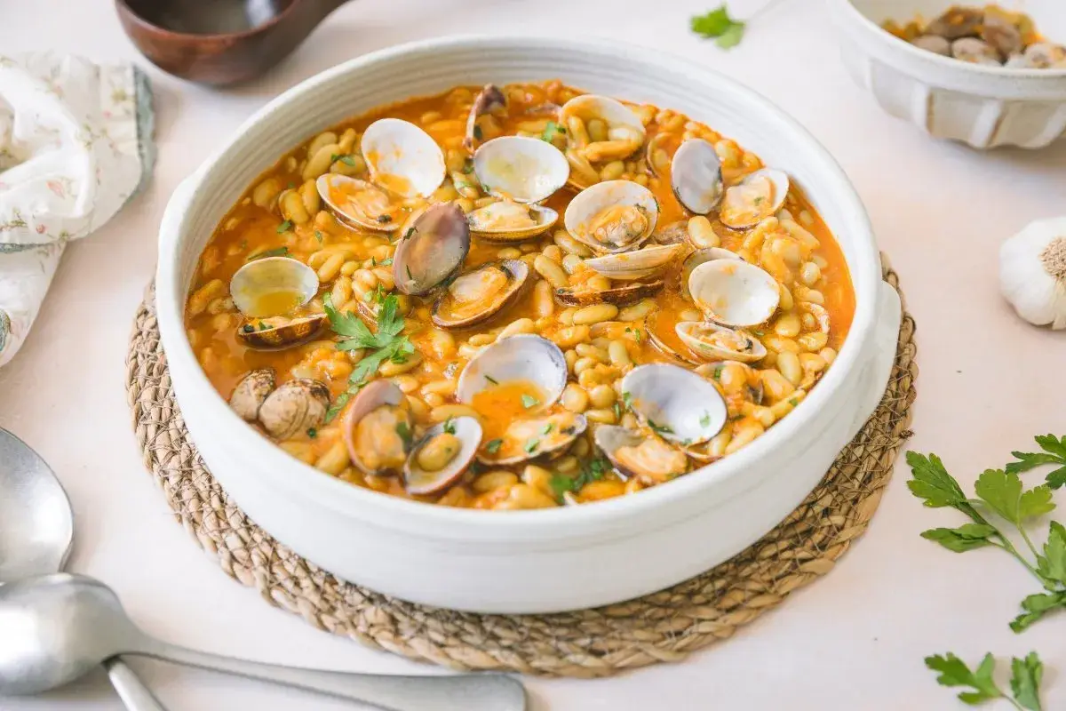 Plato de verdinas con almejas en salsa, decorado con perejil fresco. Un festín marinero y vegetal.