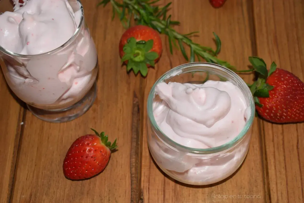Delicioso postre con fresas, cremoso y ligero, servido en copas. Fresas frescas y romero decoran la mesa de madera.