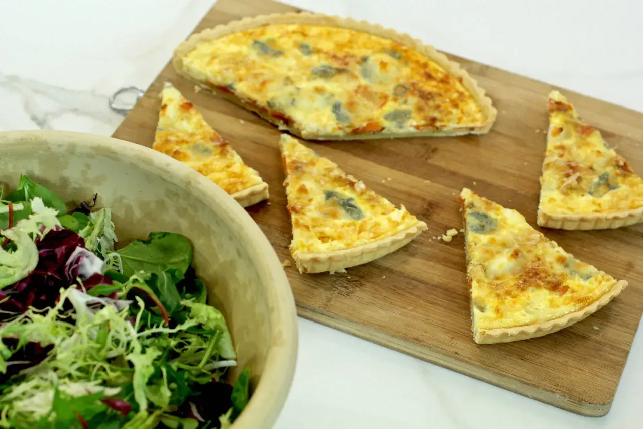 Un delicioso pastel de puerros recién horneado, cortado en porciones, junto a una ensalada fresca en un cuenco de madera.