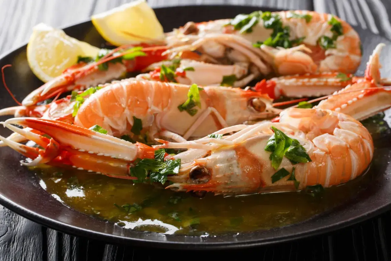 Cigalas a la plancha, jugosas y doradas, servidas con perejil picado y gajos de limón en un plato oscuro.