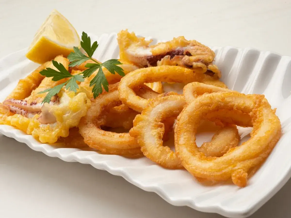 Calamares en salsa arguiñano, crujientes y dorados, servidos con limón y perejil en una fuente blanca.
