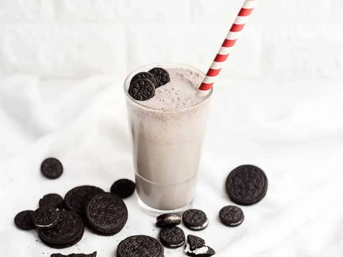 Delicioso batido de oreo cremoso, adornado con galletas enteras y trozos, listo para disfrutar con su pajita a rayas.