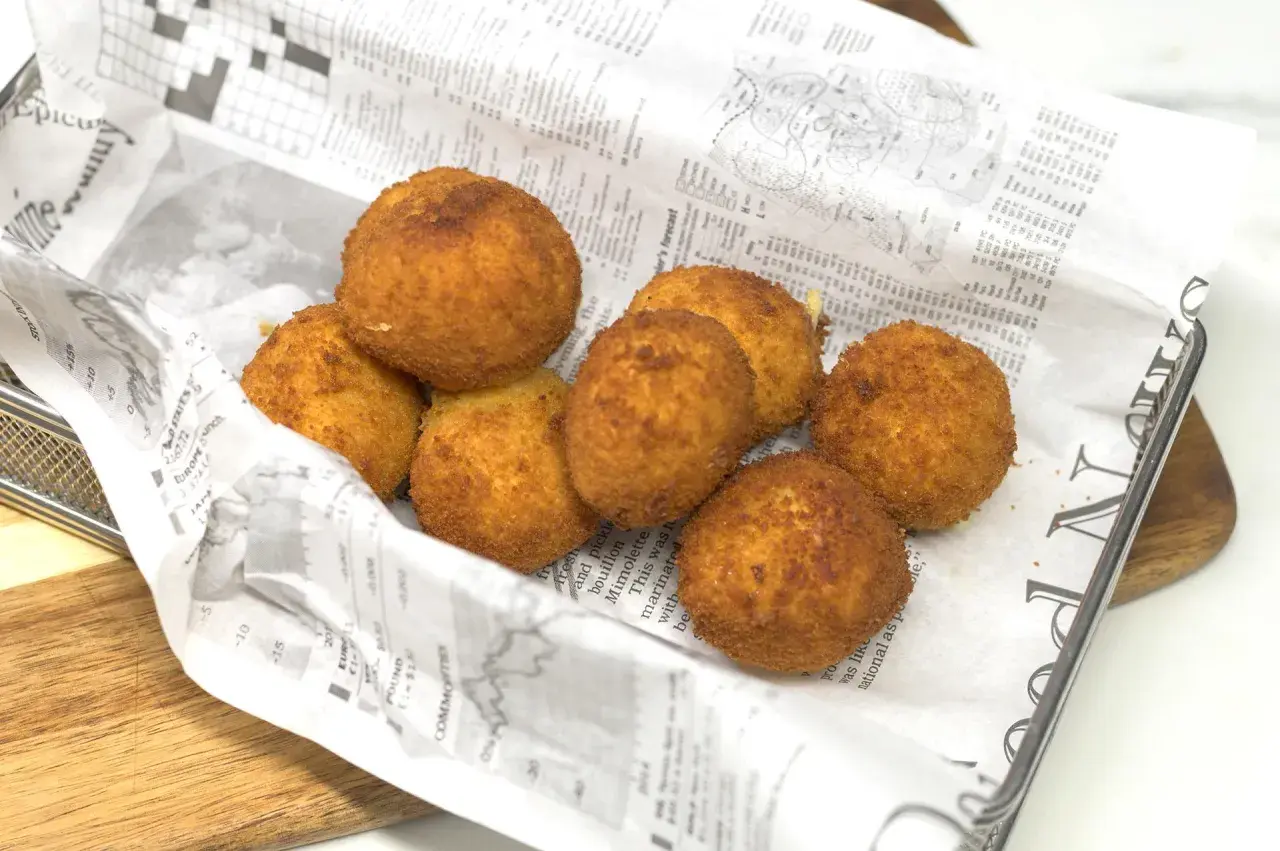 Croquetas de gambas doradas y crujientes, servidas sobre papel de periódico en una cesta metálica.