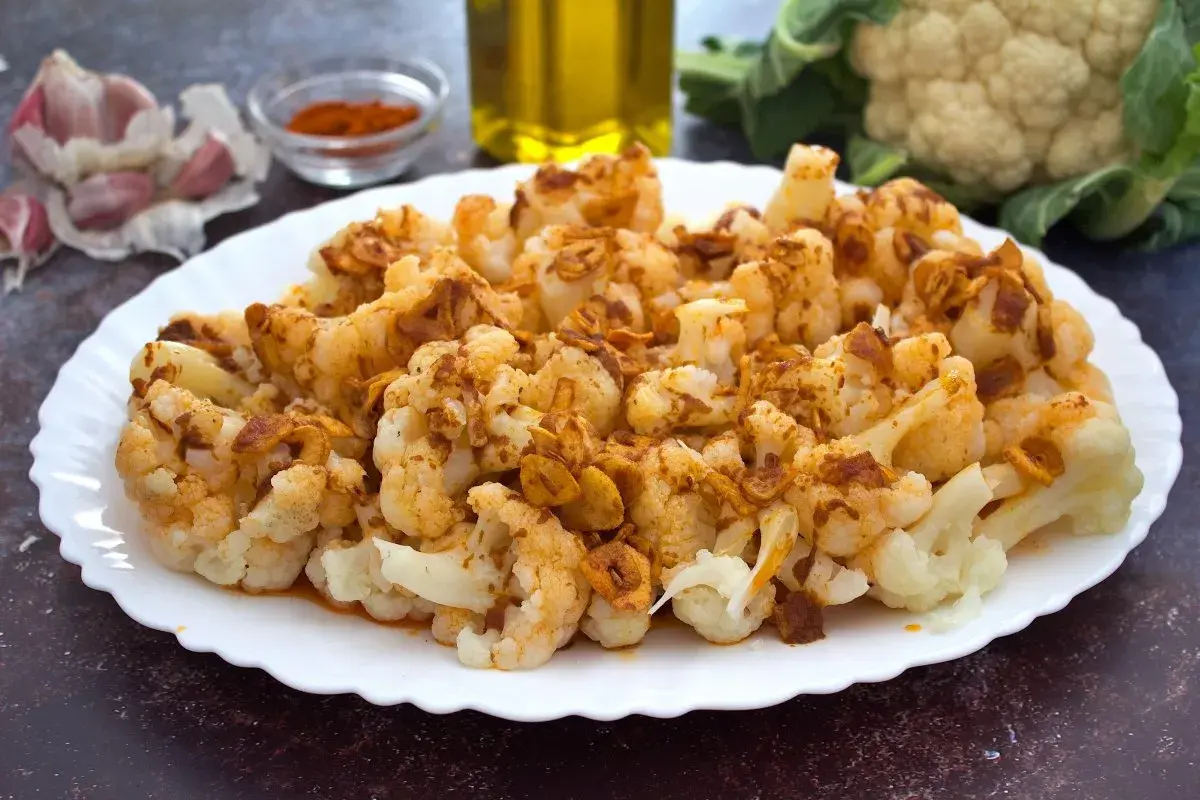 Coliflor al ajoarriero, con trozos dorados de ajo y pimentón, servida en un plato blanco.