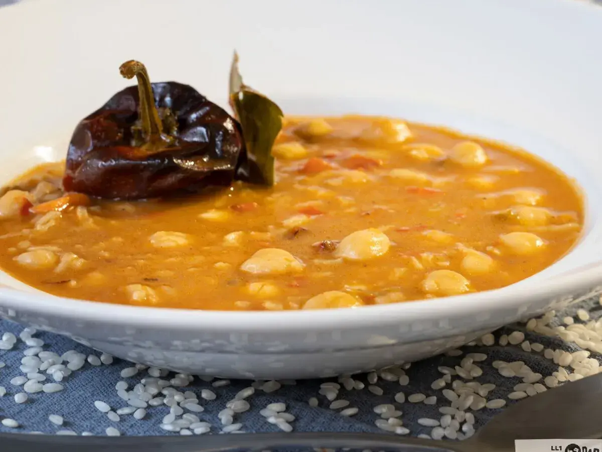 Un plato de garbanzos con arroz, reconfortante y sabroso, coronado con un pimiento seco y una hoja de laurel.