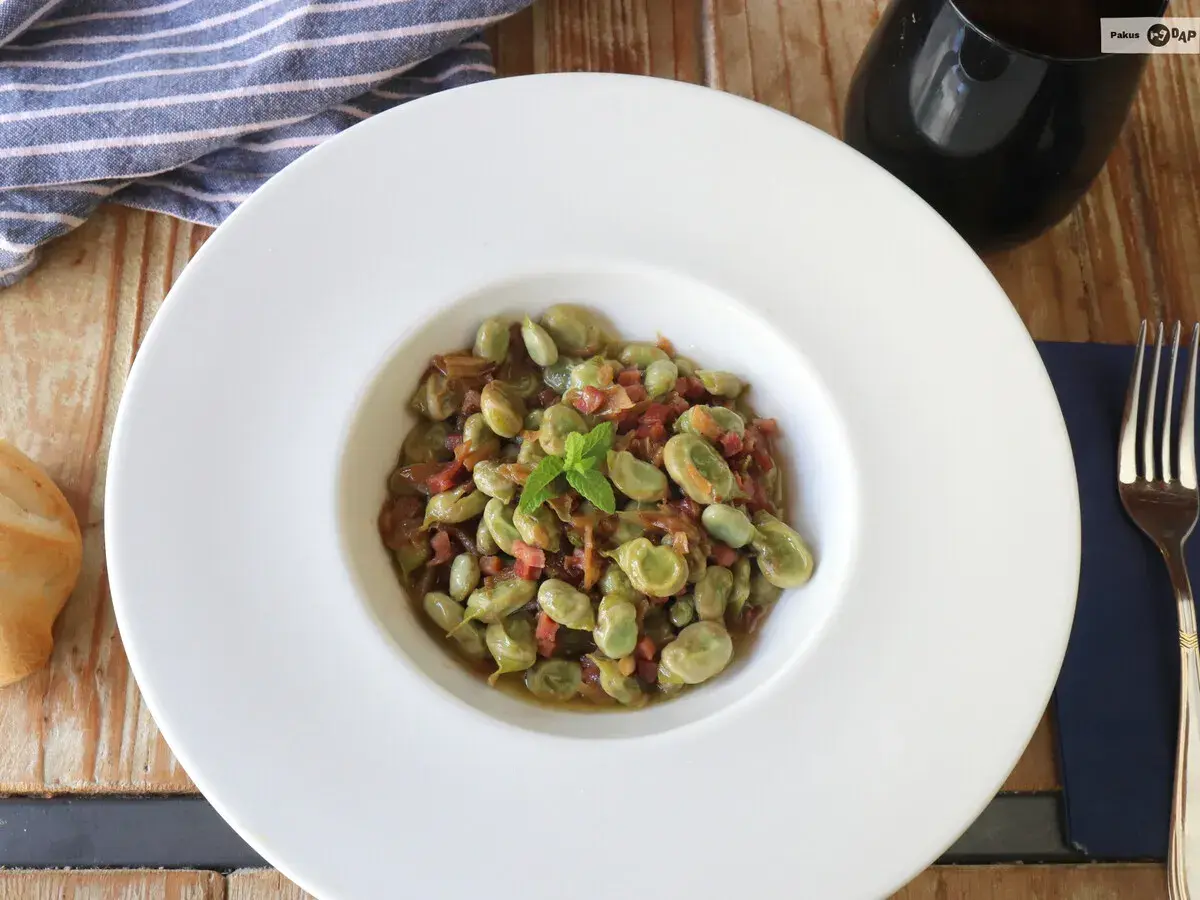 Plato de habas tiernas con jamón, ideal para tus recetas de habas. Servido en un cuenco blanco con menta fresca.