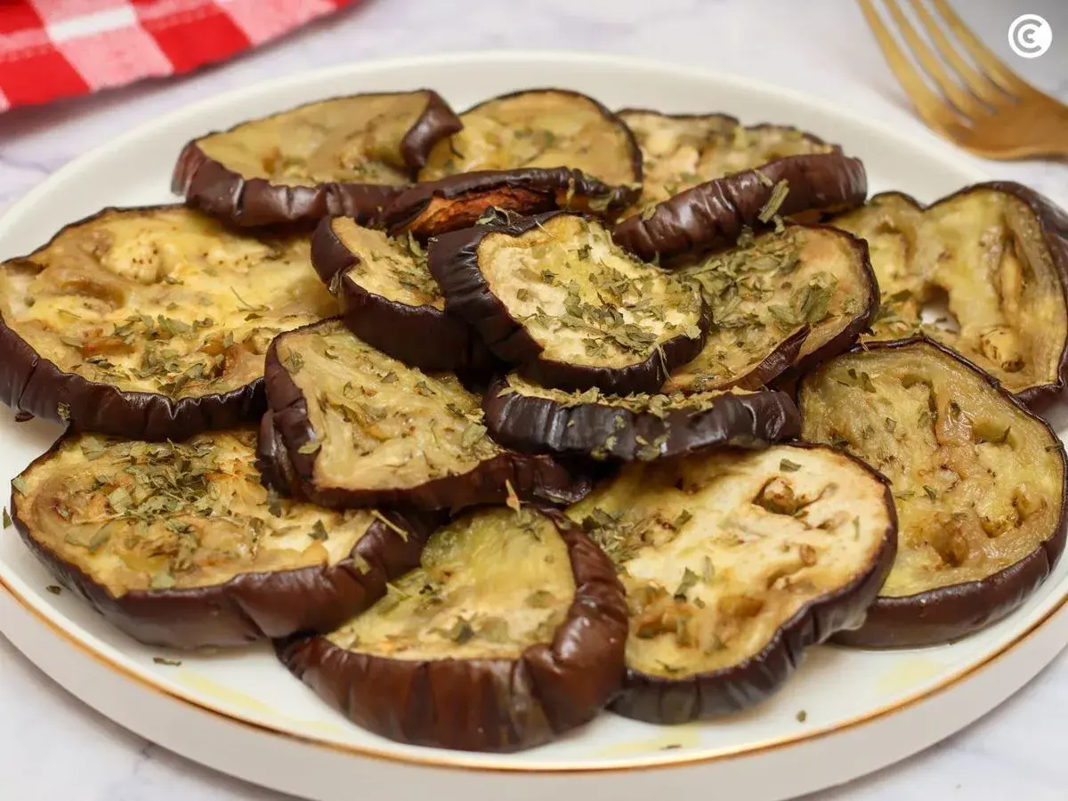 Rodajas de berenjenas al horno, doradas y espolvoreadas con hierbas aromáticas, listas para disfrutar.