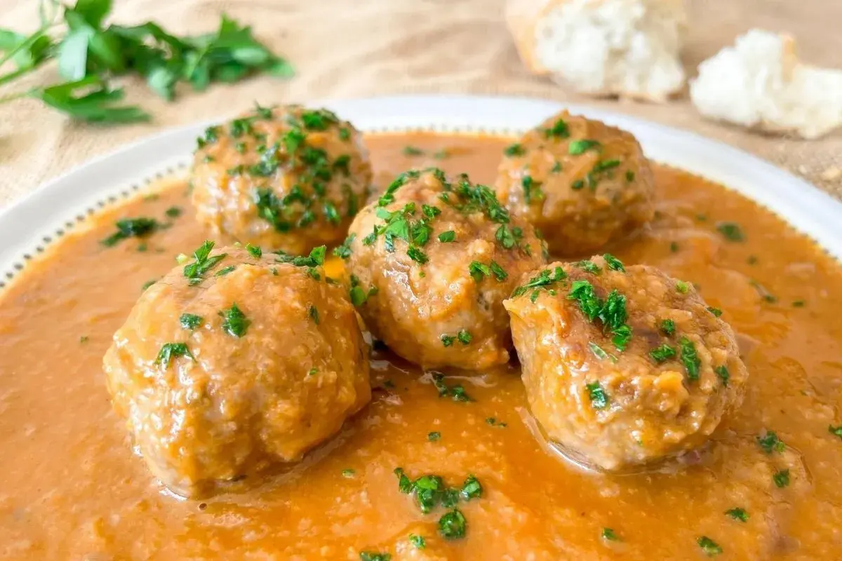 Cinco deliciosas albóndigas al horno en una rica salsa, espolvoreadas con perejil fresco. ¡Perfectas para mojar pan!