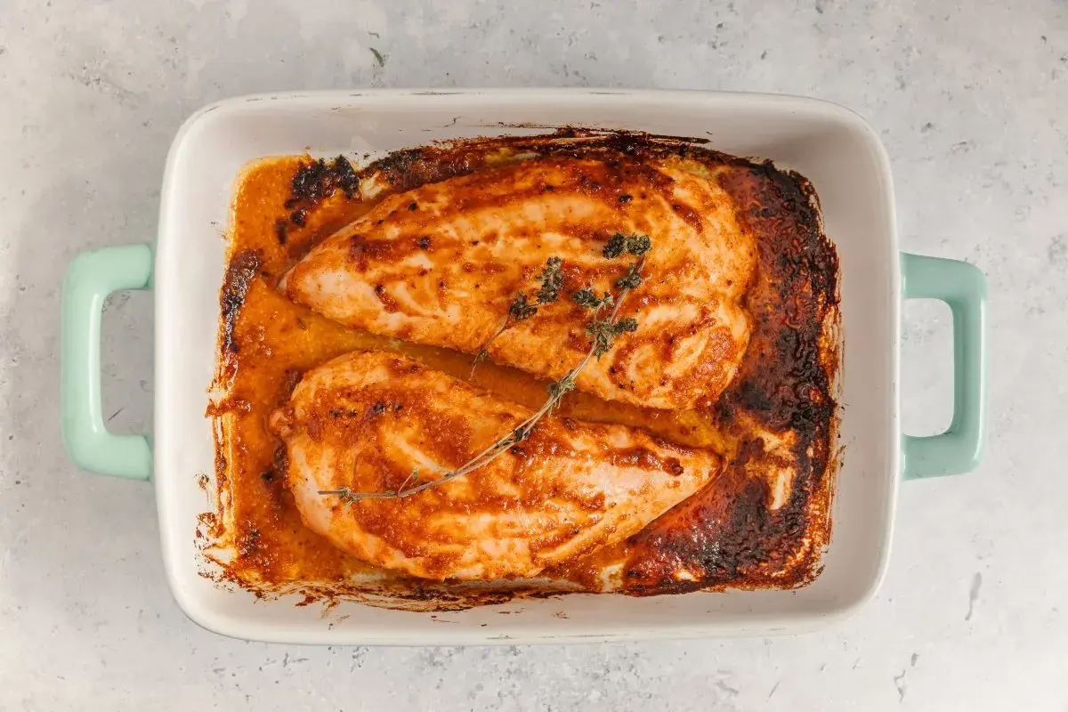Dos jugosos solomillos de pavo al horno, dorados y con hierbas, reposan en una fuente blanca con asas turquesa.