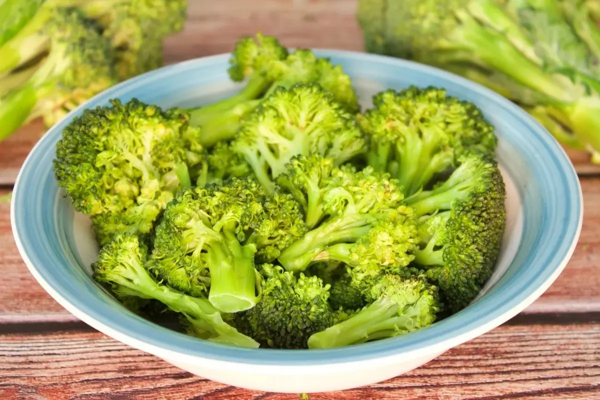 Brocoli al microondas en un cuenco azul sobre madera.
