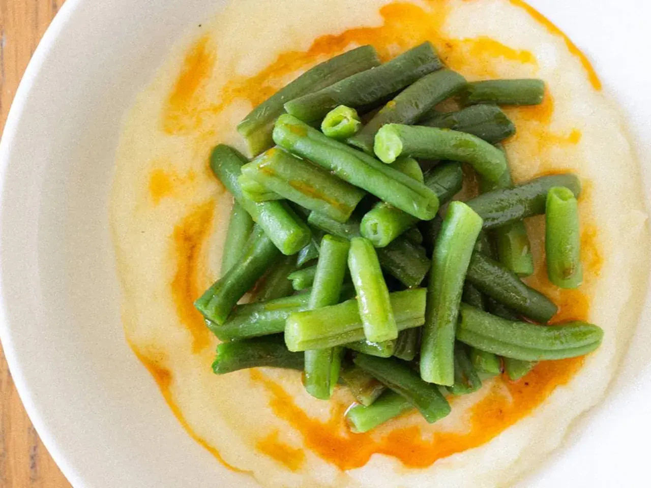 Judías verdes frescas y tiernas sobre una cremosa base de puré de patatas, con un toque de aceite de pimentón.