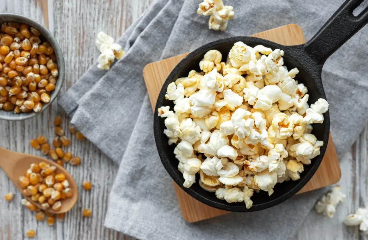 Palomitas recién hechas en sartén, listas para disfrutar. Maíz de palomitas en un cuenco y cuchara de madera.