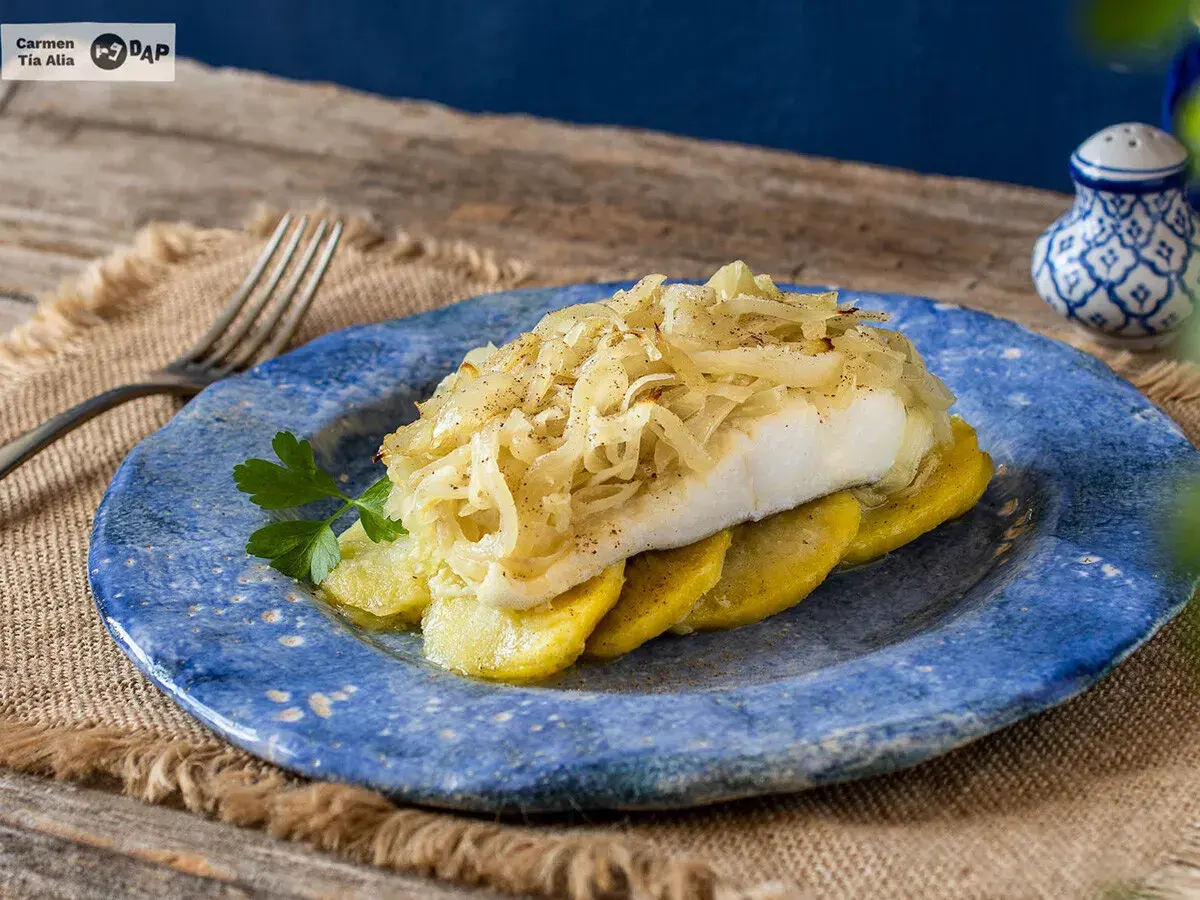Delicioso bacalao a la portuguesa, servido sobre patatas y cubierto con cebolla caramelizada.