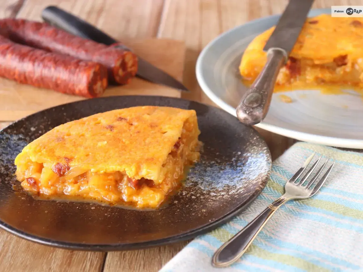 Deliciosa tortilla de chorizo, jugosa y dorada, servida en plato oscuro. Chorizos crudos al fondo.