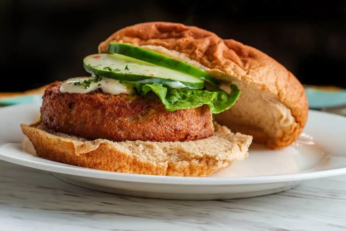 Deliciosa hamburguesa de salmón con lechuga, pepino y salsa cremosa en un pan tostado.