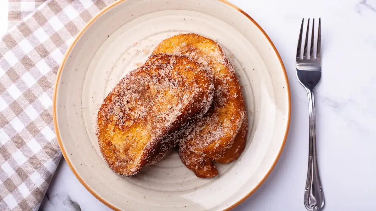 Dos torrijas doradas y azucaradas en un plato, listas para disfrutar. ¡Perfectas si las haces en Thermomix!