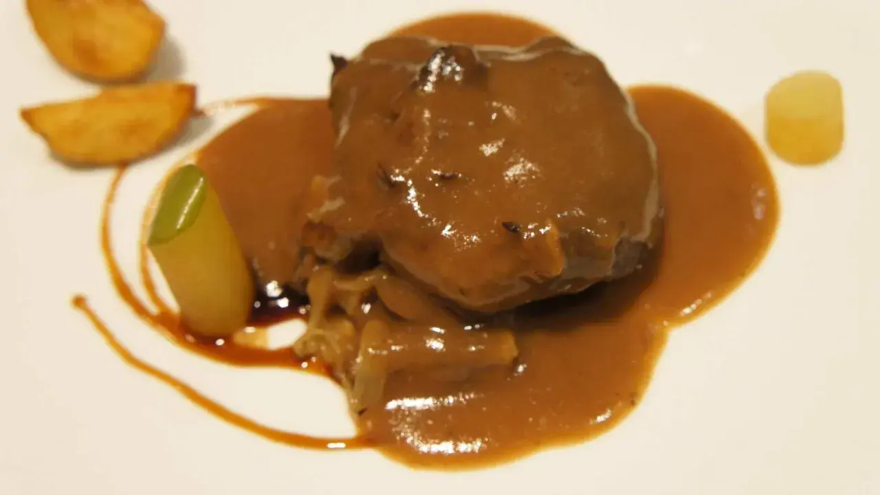 Carrilleras de ternera estofadas en salsa, acompañadas de patatas y un toque verde.