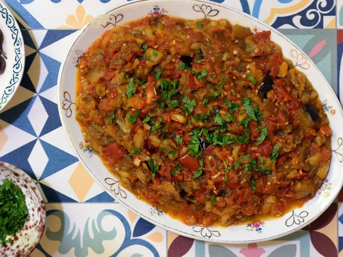 Un plato de pisto con berenjena, lleno de verduras cocidas y espolvoreado con perejil fresco.