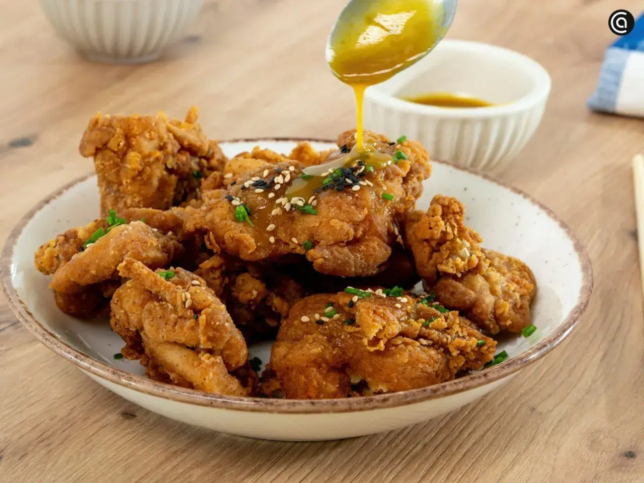 Crujiente pollo frito coreano bañado en salsa dorada, espolvoreado con semillas de sésamo y cebollín. ¡Un bocado irresistible!