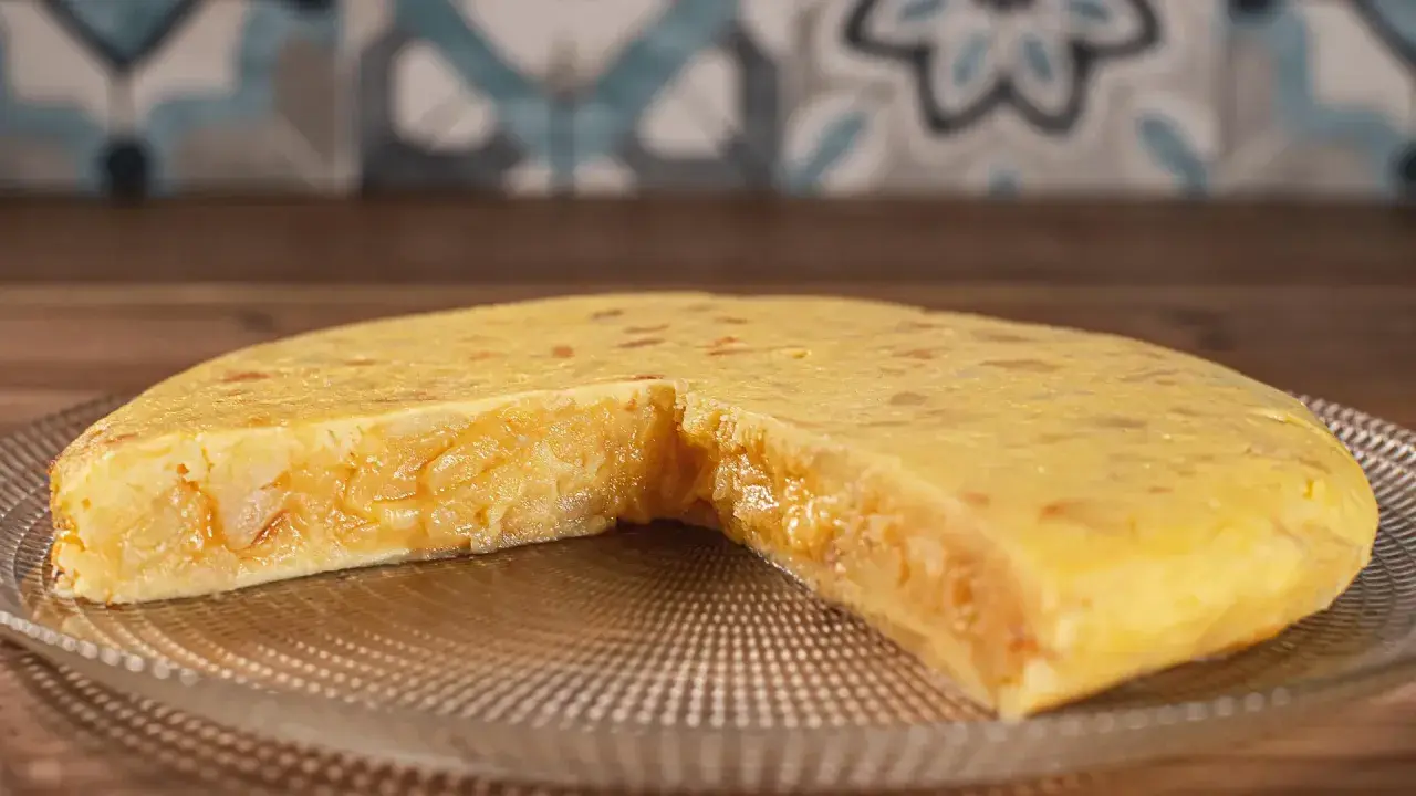 Una jugosa tortilla de patatas, con trozos de patata tierna y cebolla caramelizada, servida en un plato de cristal.