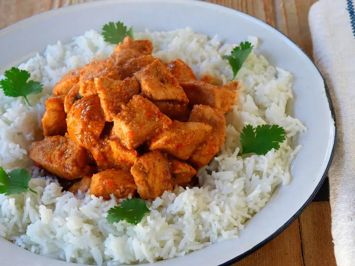 Sabroso pollo tikka masala servido sobre una cama de arroz blanco, decorado con hojas de cilantro fresco.