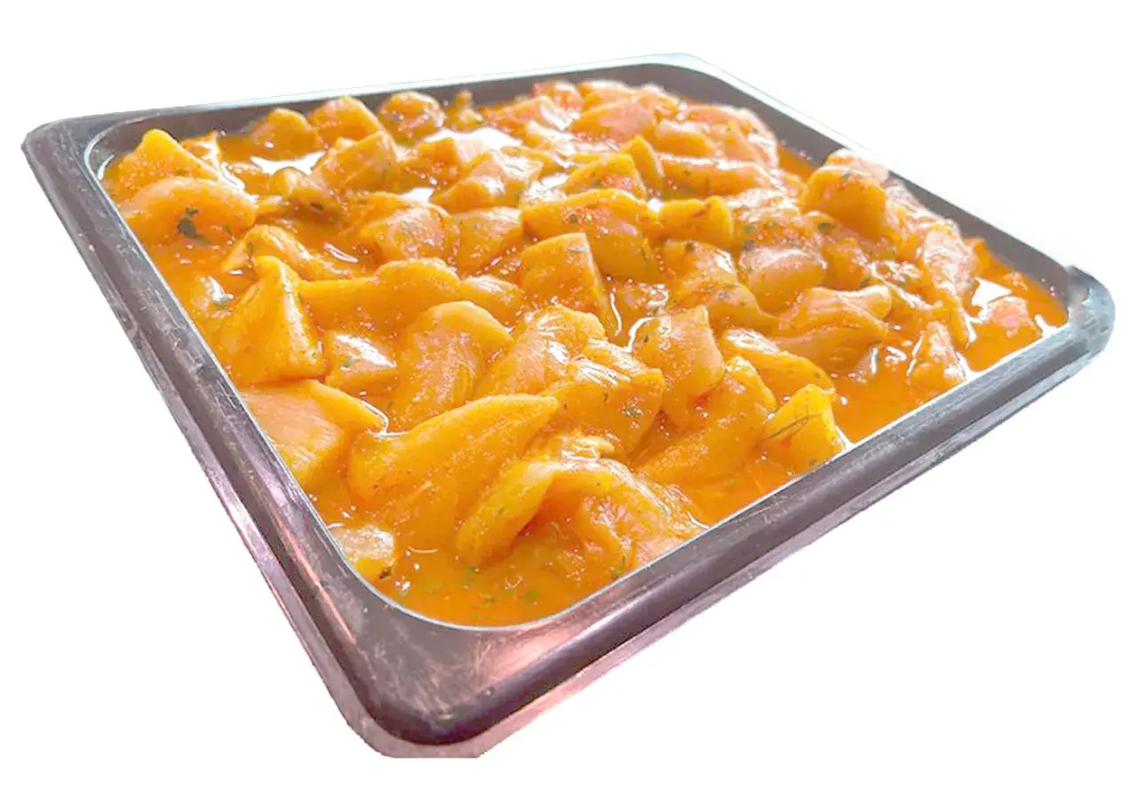 Bandeja metálica llena de trozos de pollo marinados en una salsa anaranjada, listos para convertirse en deliciosos pinchitos.