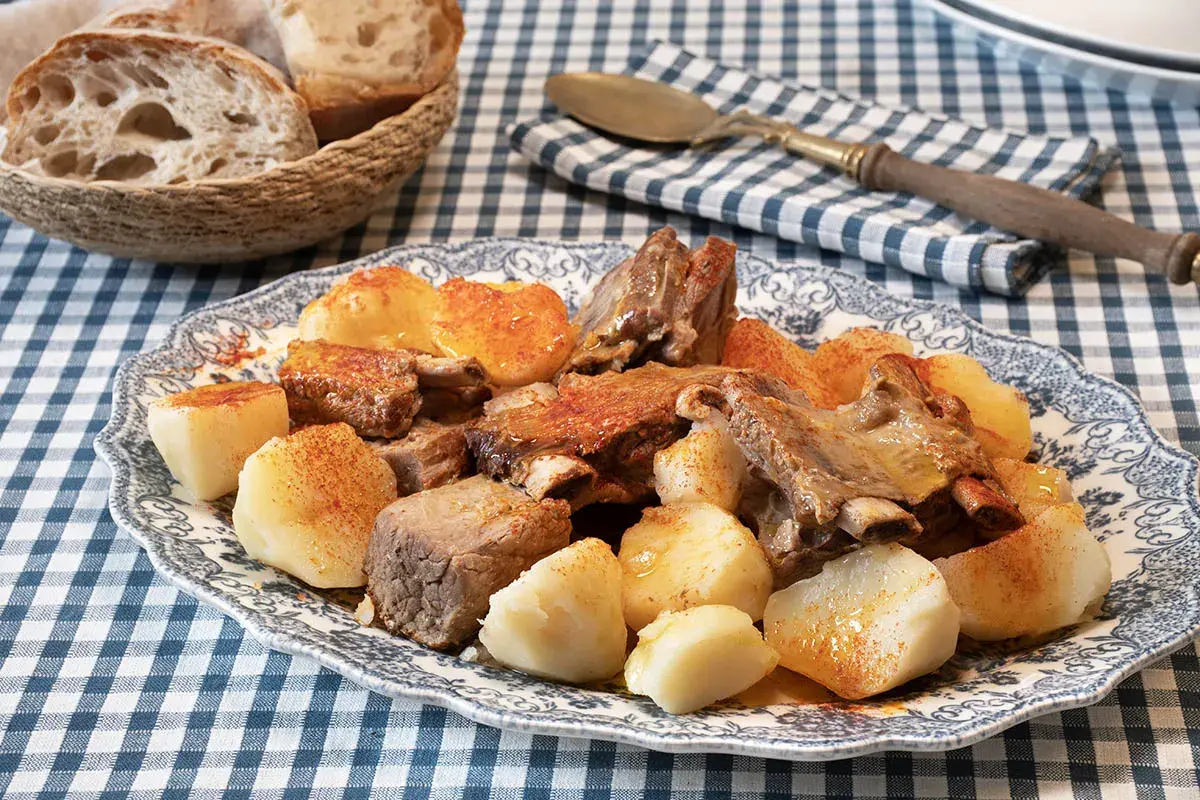 Un plato de carne o caldeiro con patatas cocidas y pan rústico en una cesta.