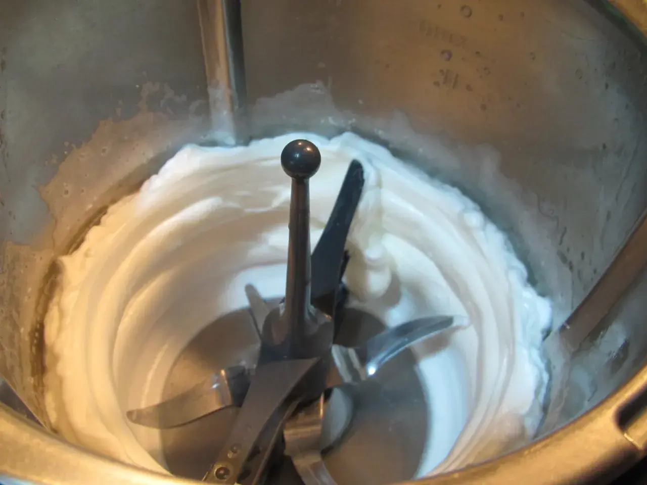 Montar claras a punto de nieve en Thermomix. La mezcla cremosa y blanca rodea las cuchillas.