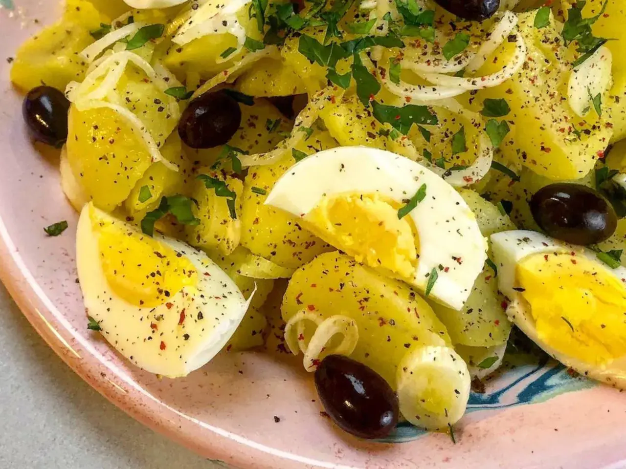 Ensalada de patatas cocidas con huevo duro, aceitunas negras y perejil. Una opción deliciosa para tus recetas con patatas cocidas.