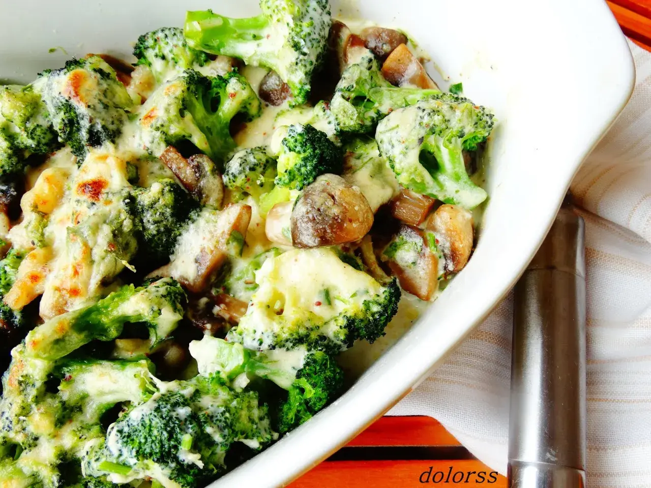Brocoli con champiñones gratinados en una cazuela blanca, cubiertos de una cremosa salsa de queso.