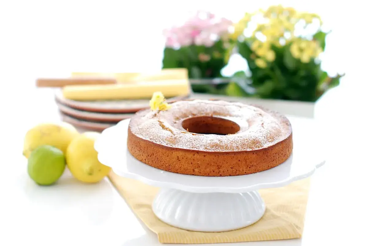 Bizcocho de limón Thermomix esponjoso y dorado, espolvoreado con azúcar glas. Limones y lima frescos al lado.