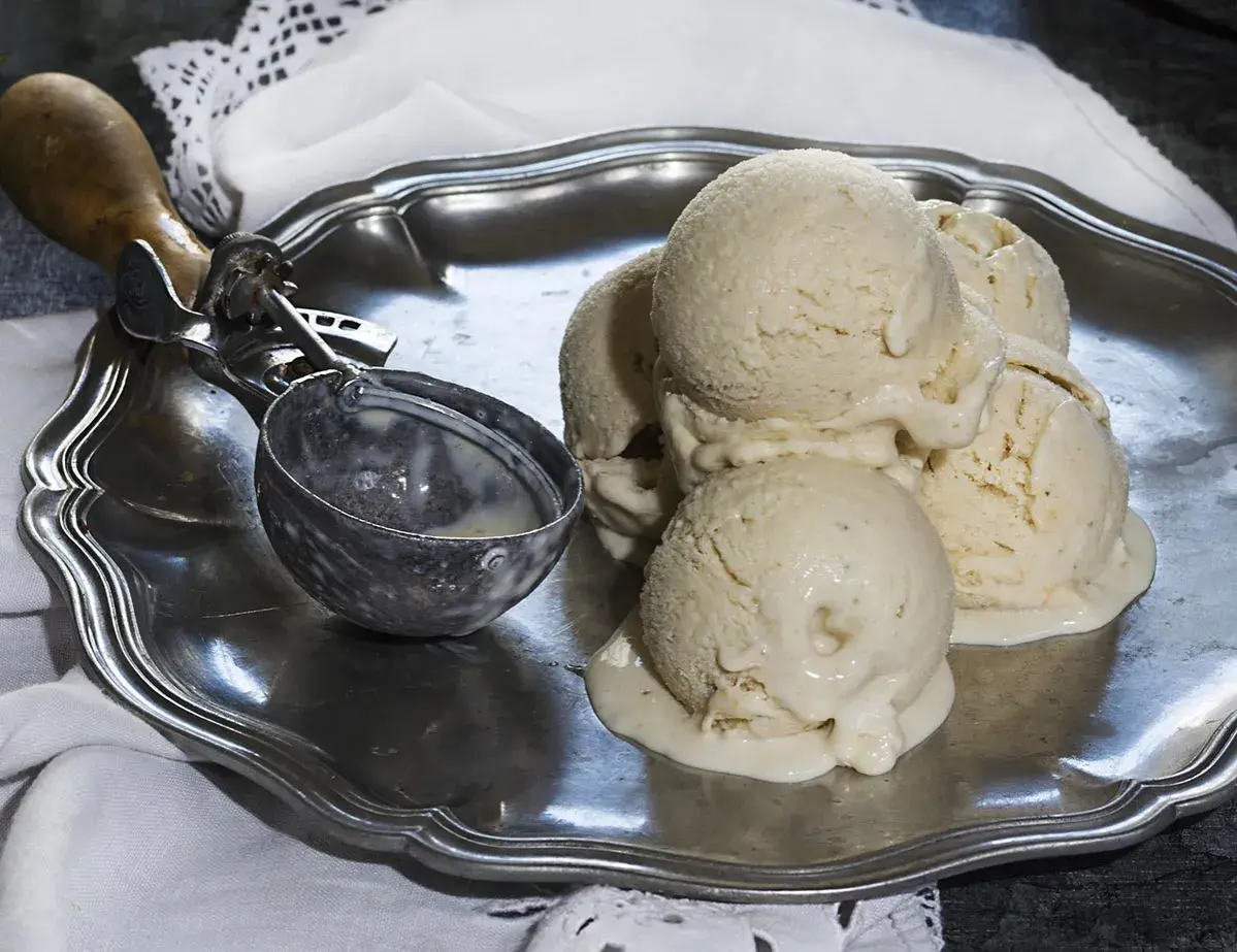Cremoso helado de plátano derritiéndose en una bandeja de plata, junto a un cucharón.